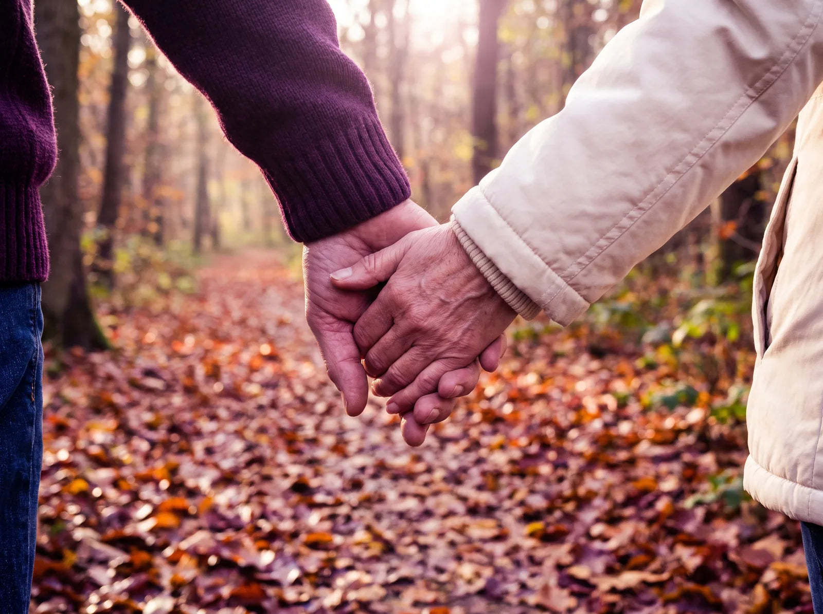 Sfeerbeeld: man en vrouw van middelbare leeftijd lopen hand in hand over een herfstpad