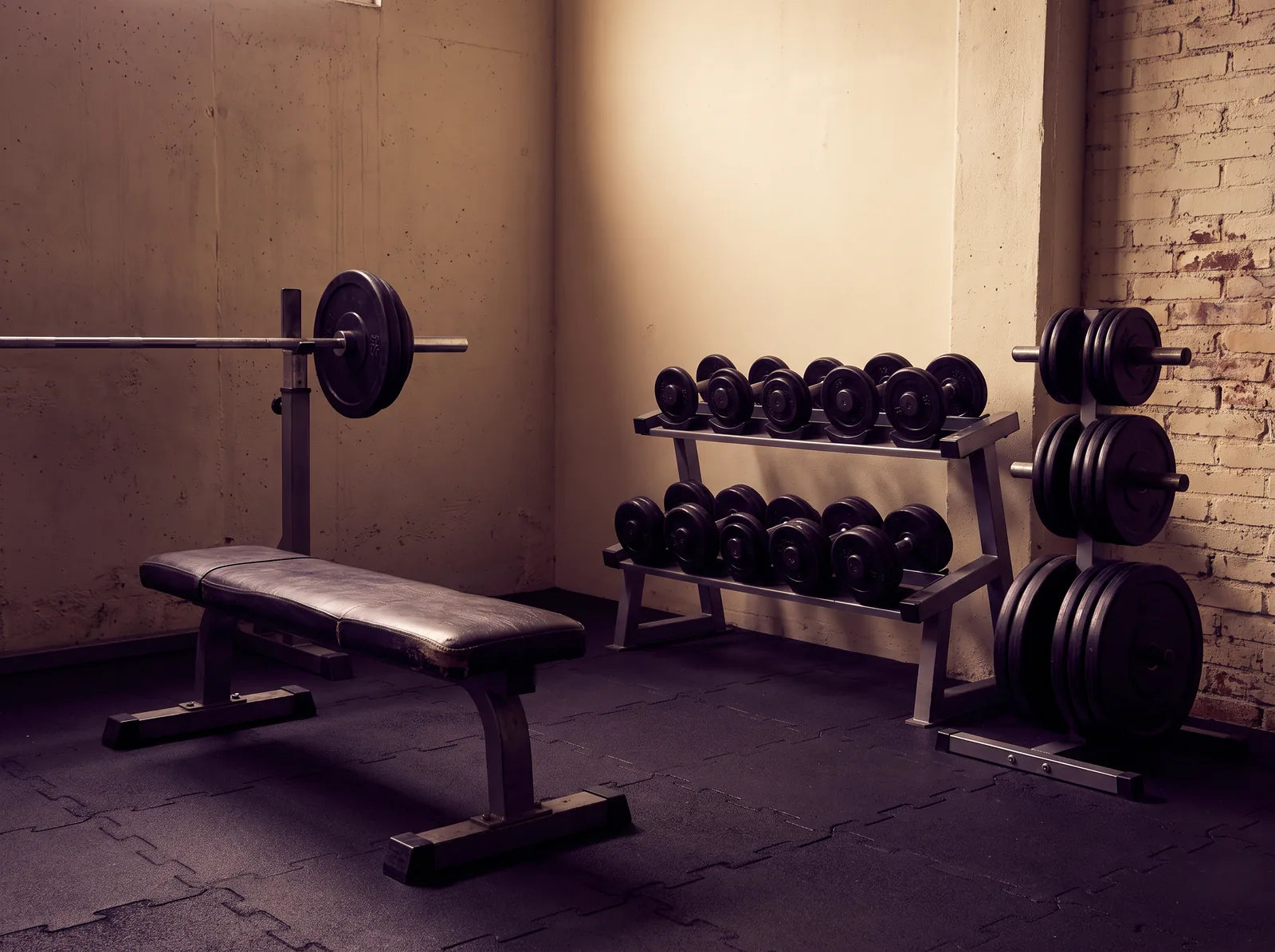 Sfeerbeeld: lege hoek van een sportschool met halterbank, dumbbells en een halterstang