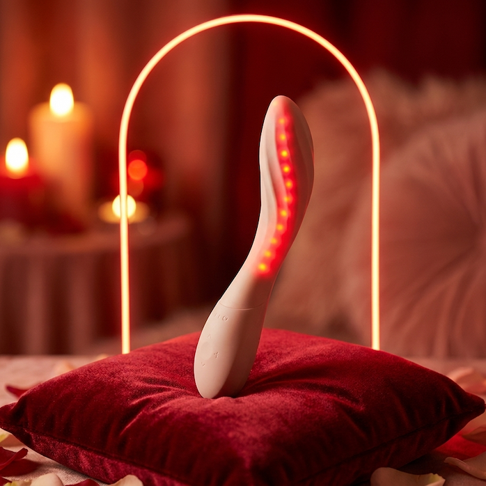 LELO Mona Spectra wellnessmassager op een rood fluwelen kussen, met roodlichtboog op de achtergrond