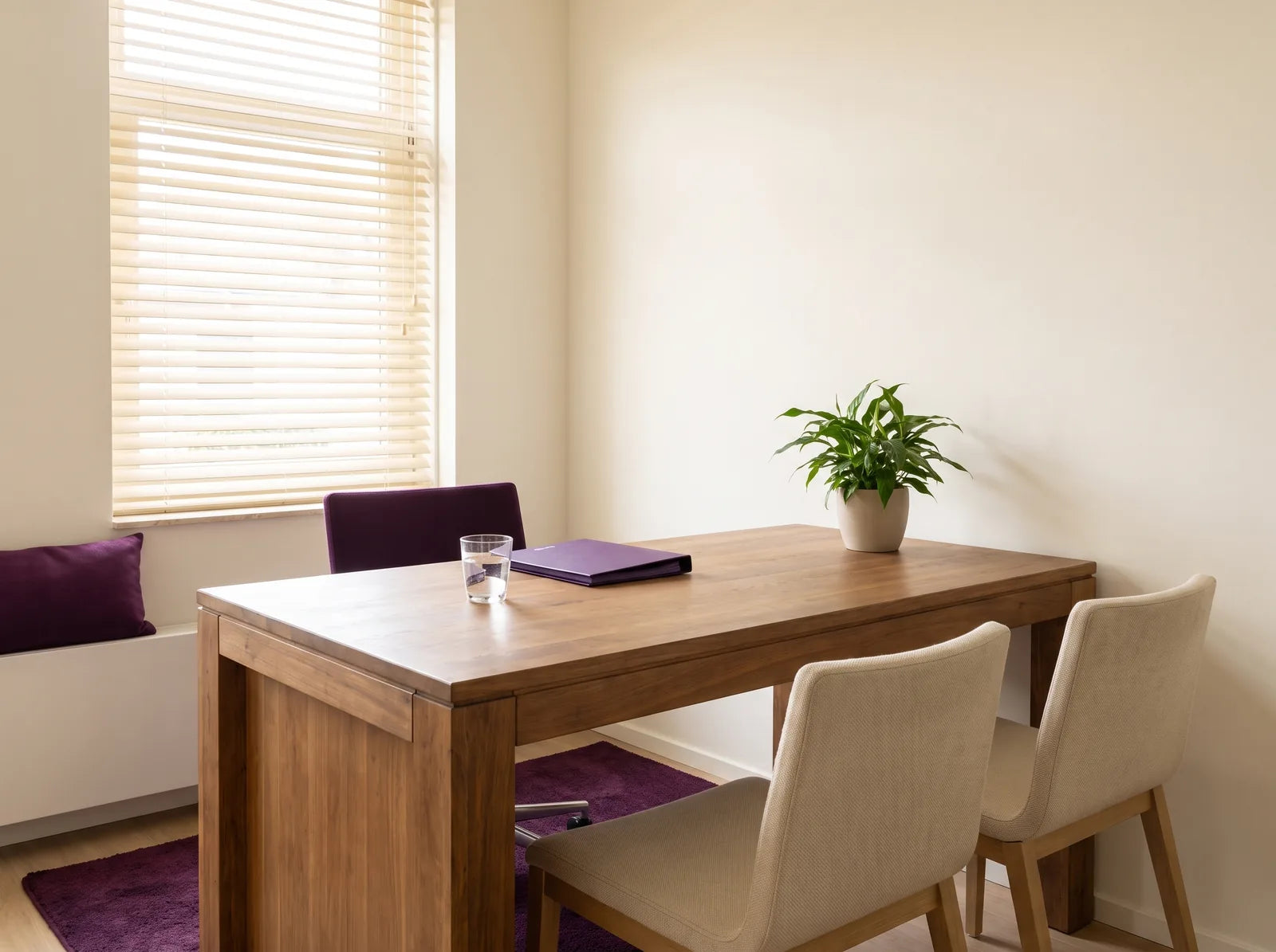 Sfeerbeeld: lichte, rustige spreekkamer met een houten tafel, drie stoelen, een plant en een glas water