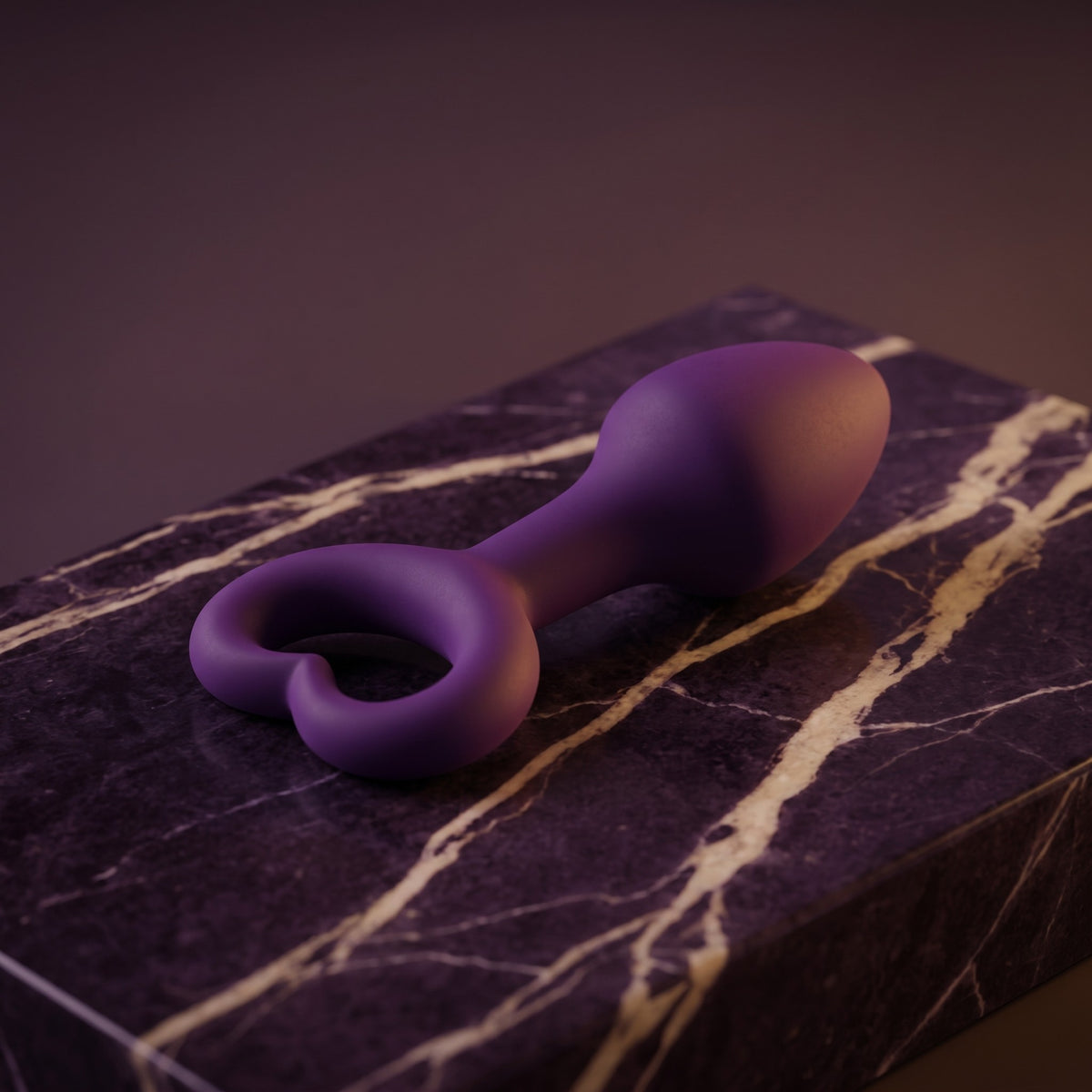 Sfeerbeeld: paarse buttplug met hartje liggend op donkerpaars marmer, gedempt licht