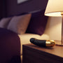 Sfeerbeeld: korte zwarte vibrator op een nachtkastje naast een brandende lamp, Dorcel Real Vibration S