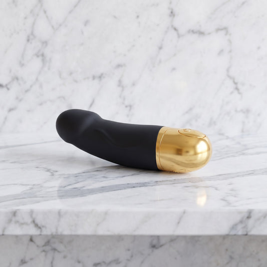 Korte zwarte vibrator met gouden onderkant op een marmeren plank, Dorcel Real Vibration S