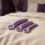 Sfeerbeeld: de drie lila dilators van Dr. Berman op een opgemaakt bed met creme linnen