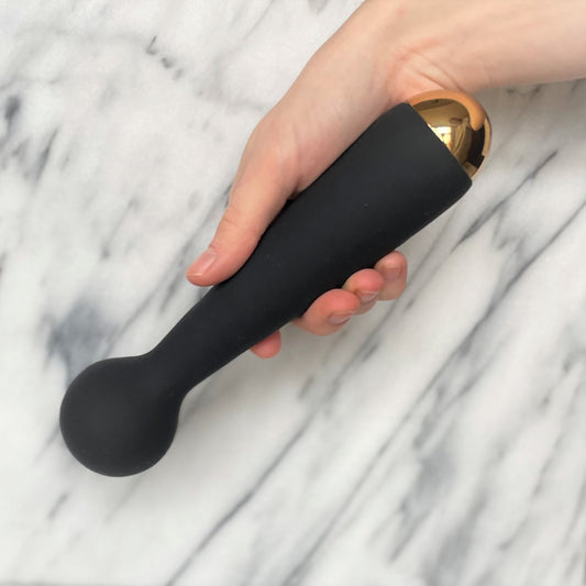 Emma Neo Wand vibrator vastgehouden in hand, slank zwart ontwerp met gouden accent