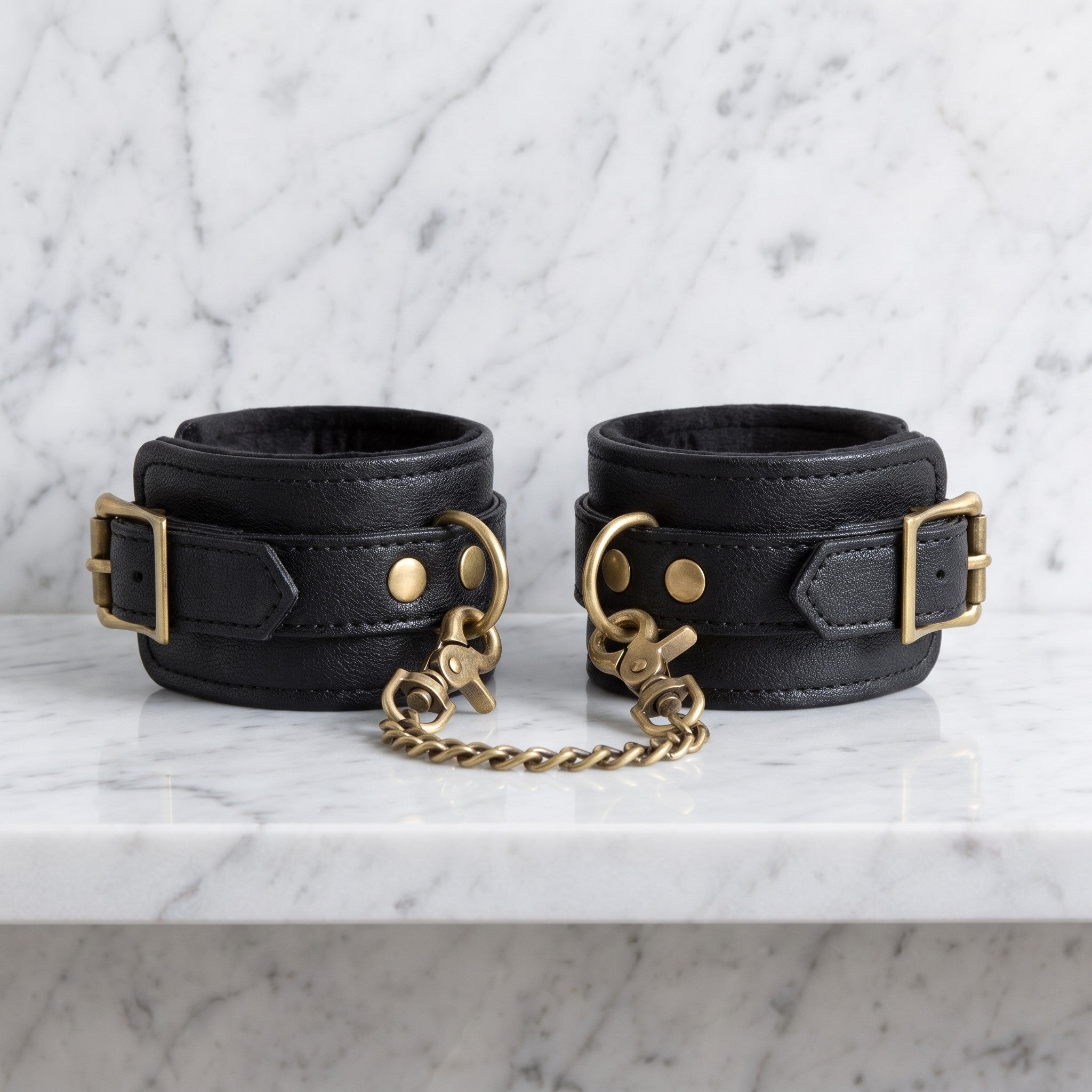 Twee zwarte enkelboeien met gouden ketting op een marmeren plank, Fifty Shades of Grey
