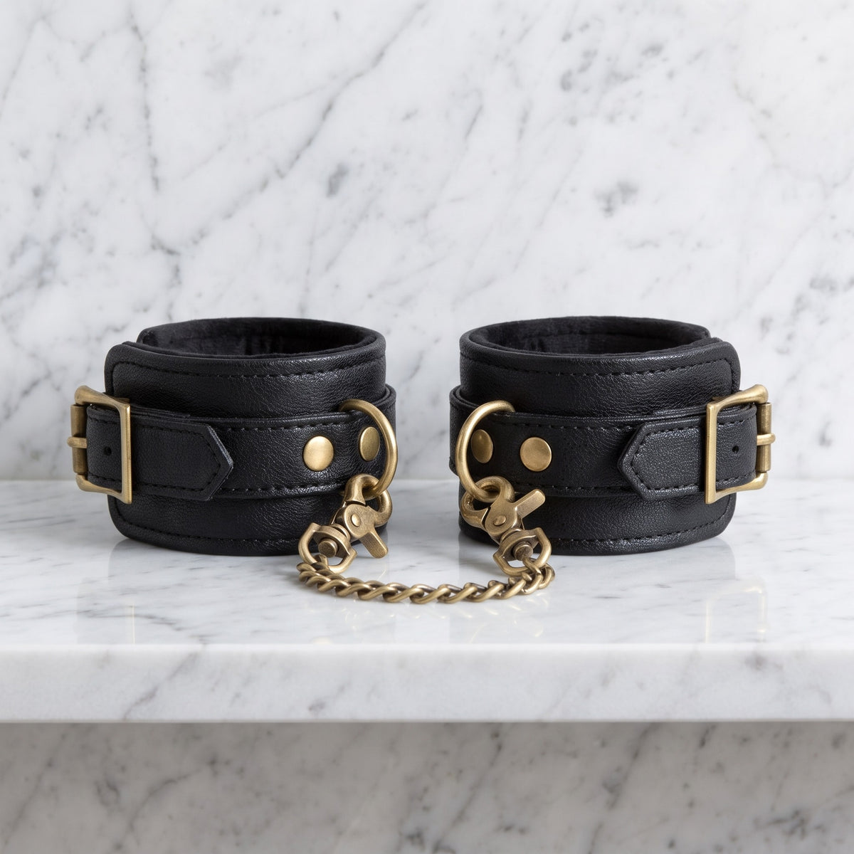 Twee zwarte enkelboeien met gouden ketting op een marmeren plank, Fifty Shades of Grey