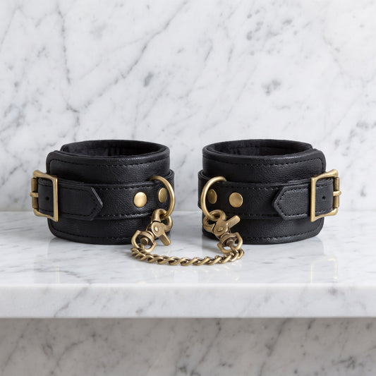 Twee zwarte enkelboeien met gouden ketting op een marmeren plank, Fifty Shades of Grey