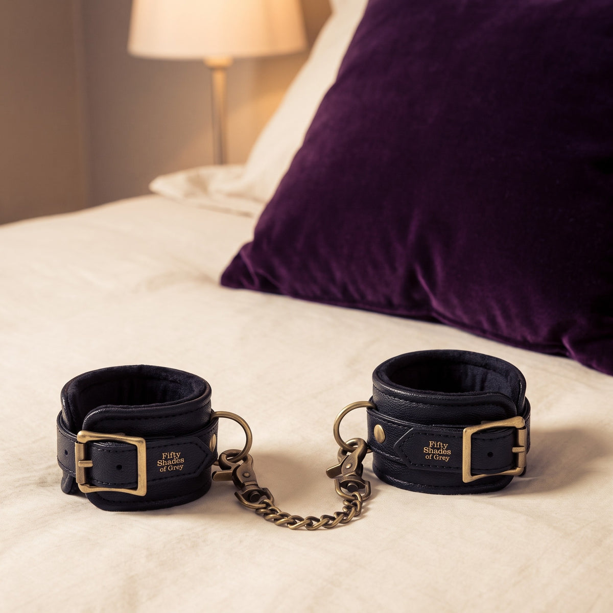 Sfeerbeeld: Fifty Shades of Grey handboeien op creme linnen naast een paars kussen
