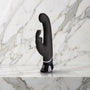Zwarte Greedy Girl rabbit vibrator met gebogen kop en oortjes rechtop op een marmeren plank