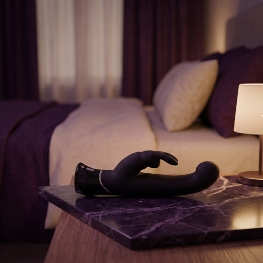Sfeerbeeld: zwarte Greedy Girl rabbit vibrator liggend op donkerpaars marmer bij gedempt lamplicht