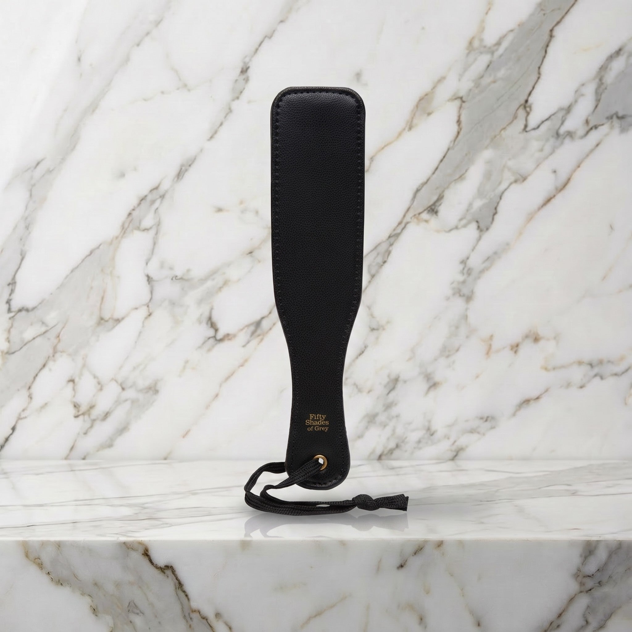 Kleine zwarte spanking paddle met hanglus rechtop op een marmeren plank, Fifty Shades