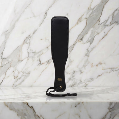 Kleine zwarte spanking paddle met hanglus rechtop op een marmeren plank, Fifty Shades