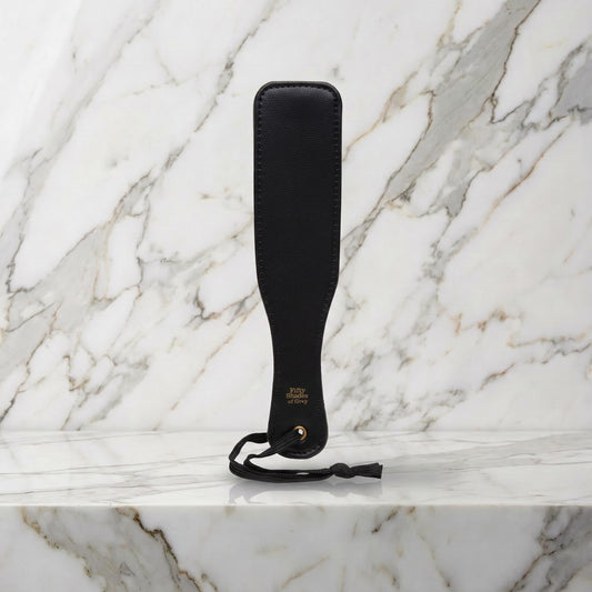 Kleine zwarte spanking paddle met hanglus rechtop op een marmeren plank, Fifty Shades