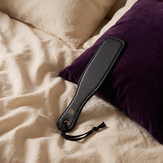 Sfeerbeeld: zwarte paddle op een bed met crème linnen tegen een paars fluwelen kussen