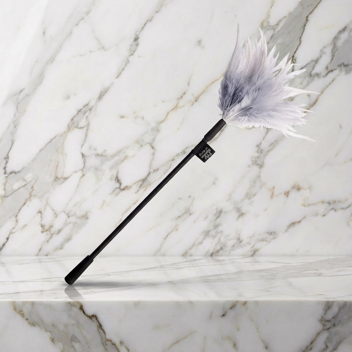 Fifty Shades Tease streelveer met lichtgrijze veren en zwarte steel op een marmeren plank