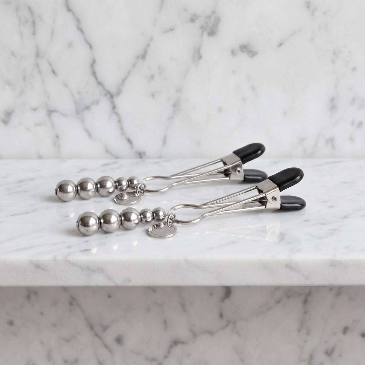 Twee zilverkleurige The Pinch tepelklemmen met kralen op een marmeren plank, Fifty Shades of Grey