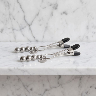Twee zilverkleurige The Pinch tepelklemmen met kralen op een marmeren plank, Fifty Shades of Grey
