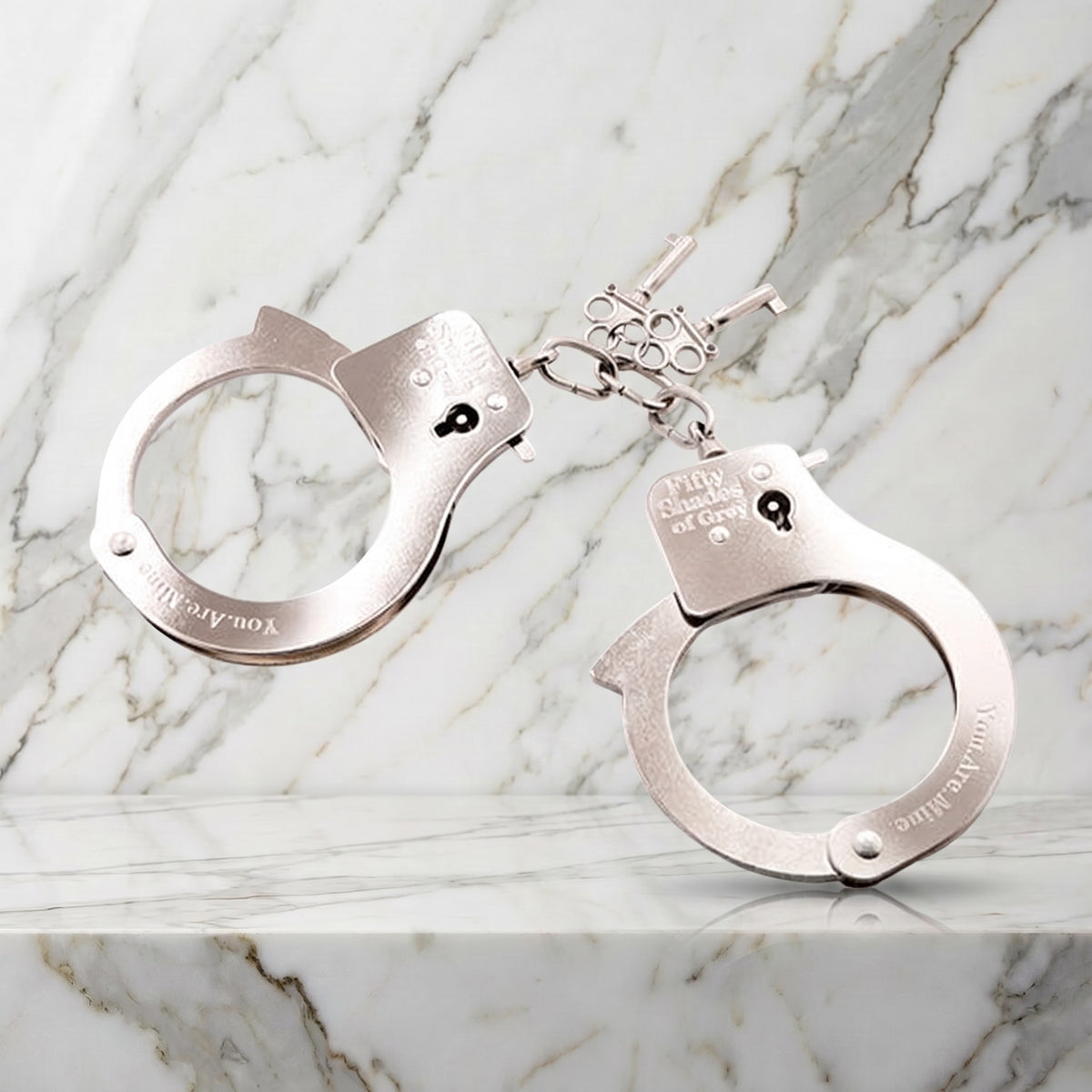 Zilveren metalen handboeien met sleuteltjes op een marmeren plank, You Are Mine van Fifty Shades
