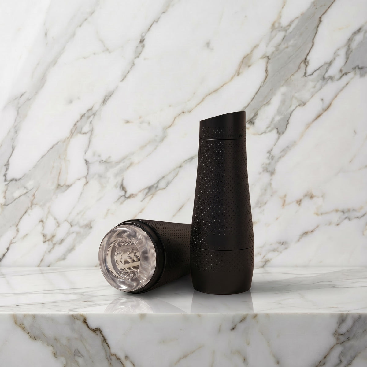 Zwarte Fleshlight Flight Pilot koker rechtop op een marmeren plank met de losse doorzichtige huls ernaast
