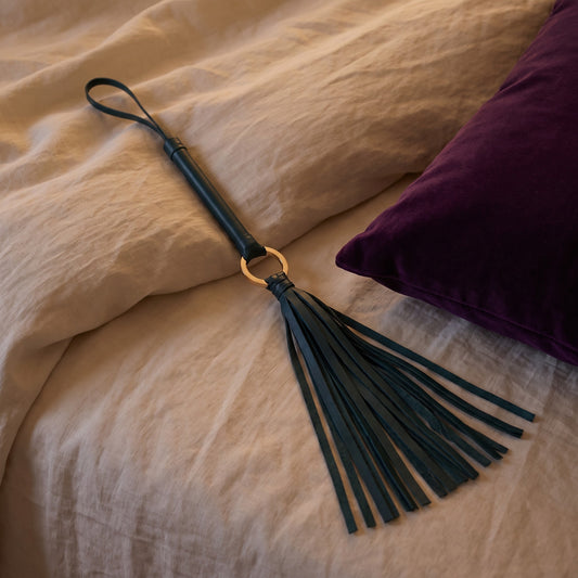 Sfeerbeeld: groene flogger op een bed met creme linnen naast een paars kussen