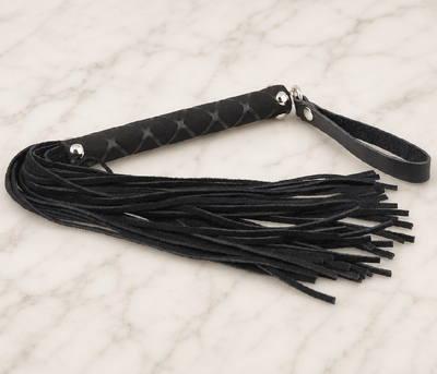 Kleine zwarte flogger met leren strengen en polslus op een marmeren plank