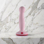 Licht roze Fun Factory Amor dildo met rode zuigvoet rechtop op een marmeren plank