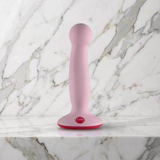 Licht roze Fun Factory Amor dildo met rode zuigvoet rechtop op een marmeren plank