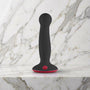 Zwarte Fun Factory Amor dildo met rode zuigvoet rechtop op een marmeren plank