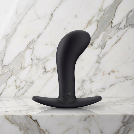 Zwarte gebogen buttplug Bootie Large met T-voet op een marmeren plank, Fun Factory