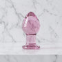 Roze doorzichtige glazen buttplug rechtop op een marmeren plank, van Gildo