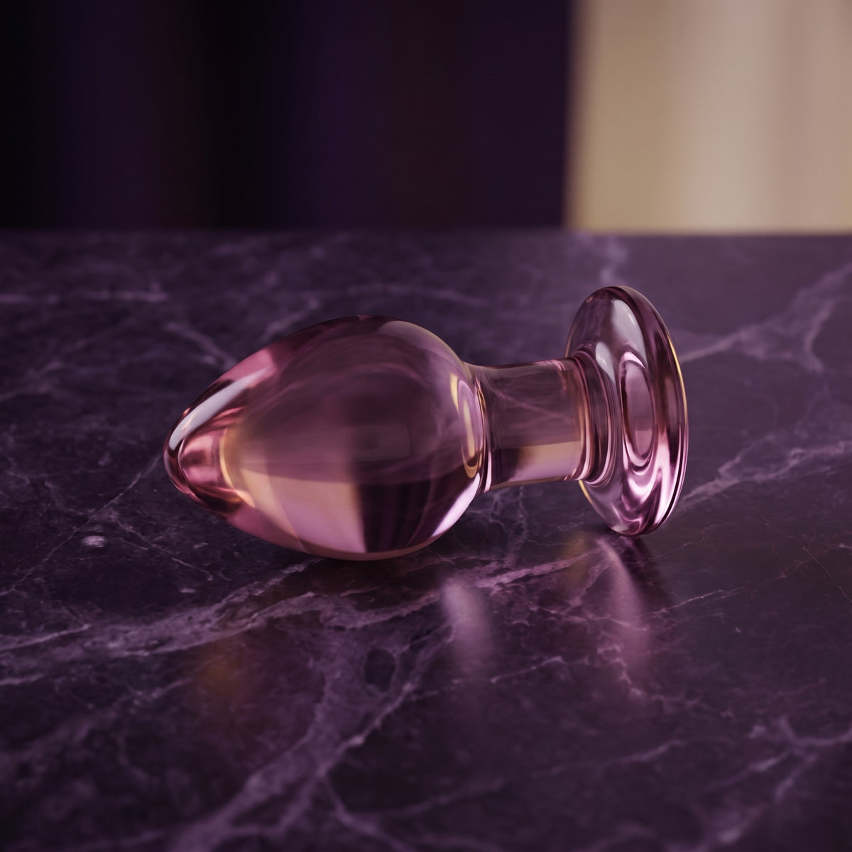 Sfeerbeeld: roze glazen buttplug van Gildo liggend op donkerpaars marmer in gedempt licht