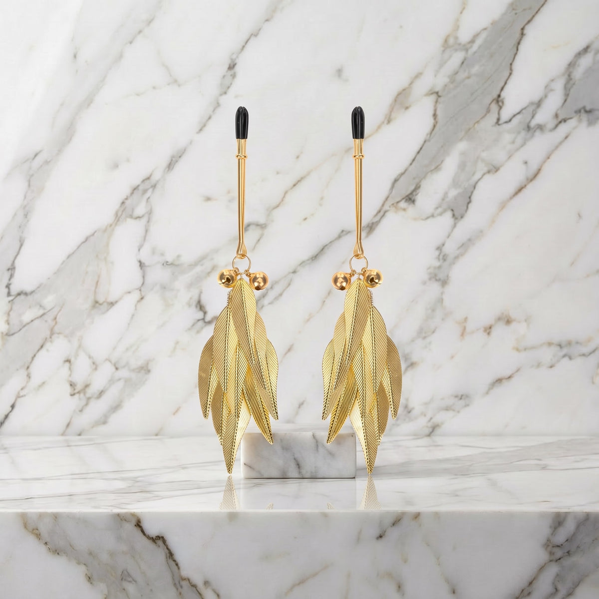 Twee goudkleurige tepelklemmen met gouden veertjes op een marmeren plank