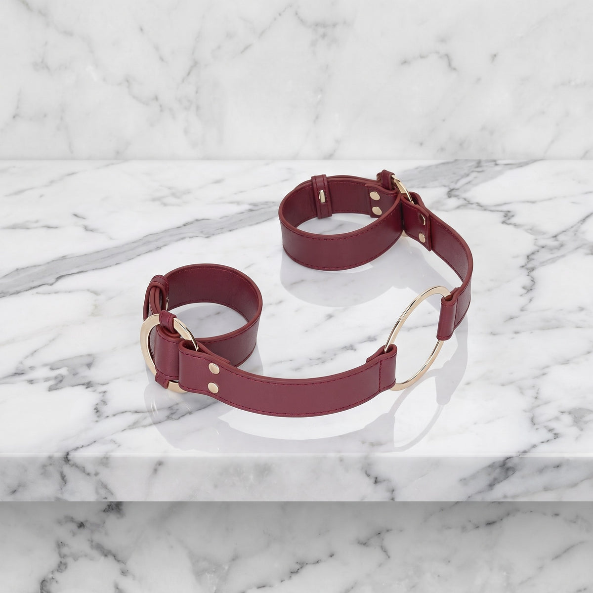 Burgundy handboeien met gouden ring en lange band op een marmeren plank, Ouch! Halo