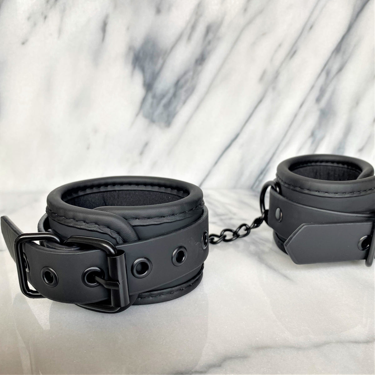 Zwarte vegan leren handboeien close-up met gesp, ketting en zachte voering op marmer