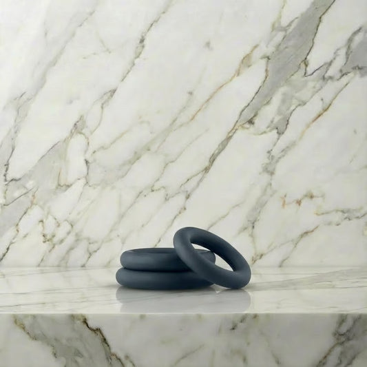 Drie donkergrijze siliconen cockringen in verschillende maten op marmeren plank