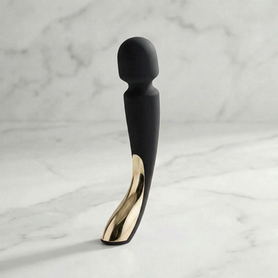 Zwarte Smart Wand Large 2 met goudkleurige handgreep op een marmeren plank, Lelo