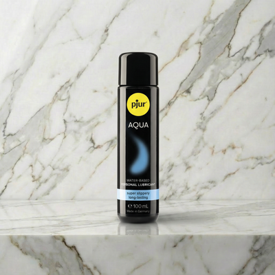 Fles Pjur Aqua glijmiddel op waterbasis van 100 ml op een marmeren plank