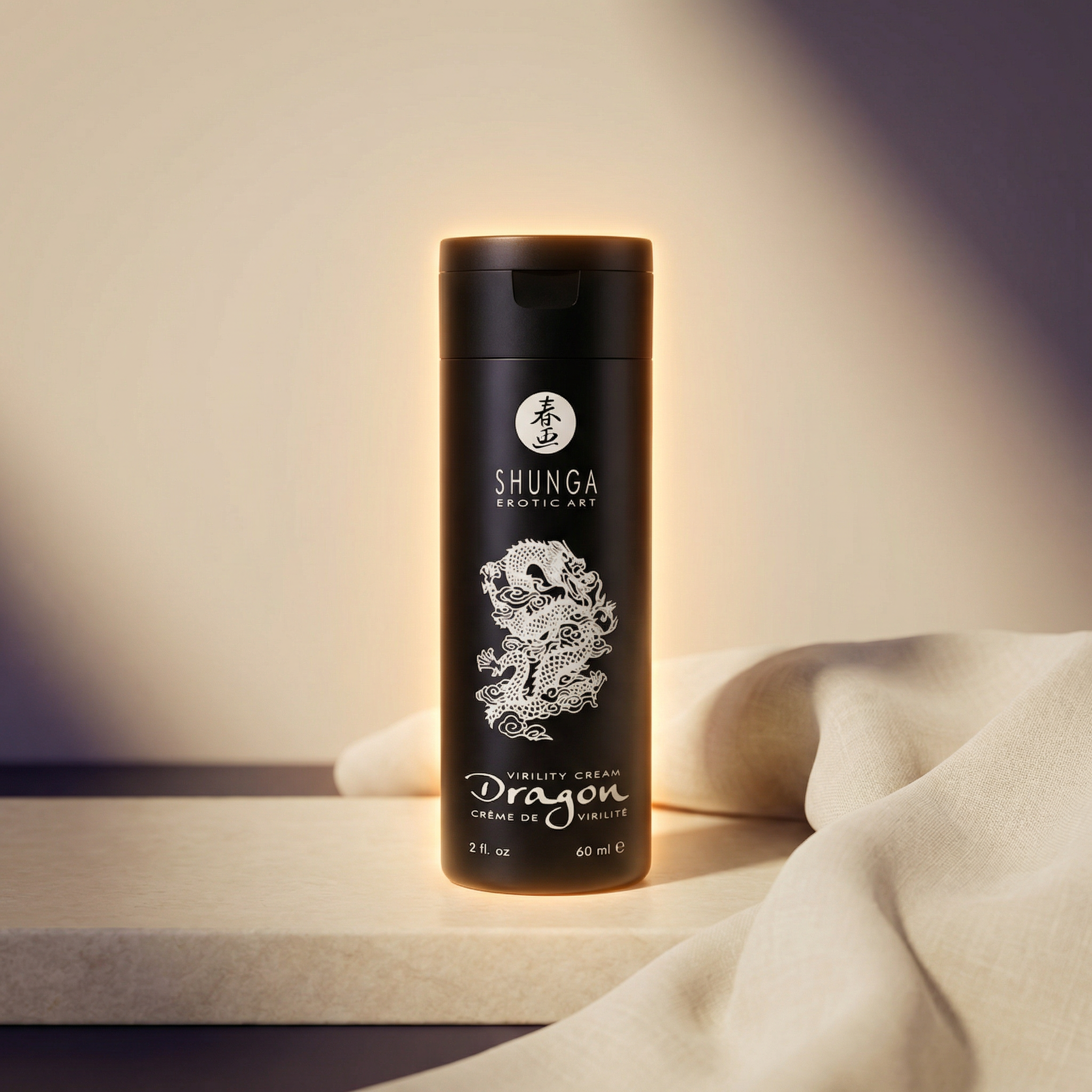 Sfeerbeeld: flesje Shunga Dragon crème in warm licht naast een creme doek