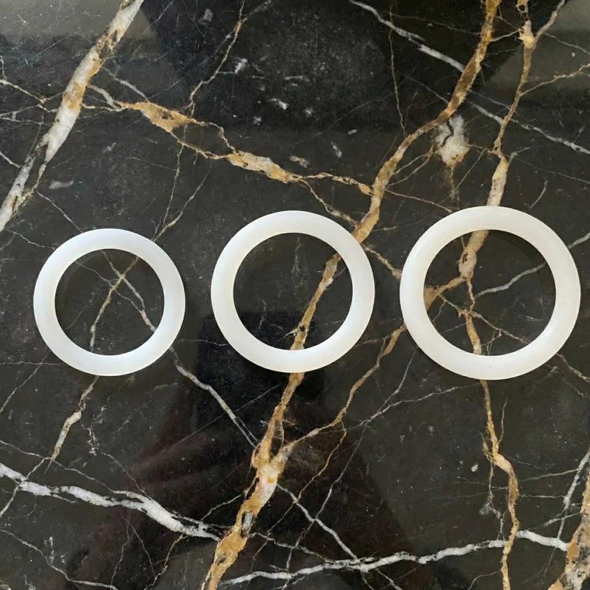 Sfeerbeeld van drie witte siliconen cockringen op donker marmer, White Cockring Set