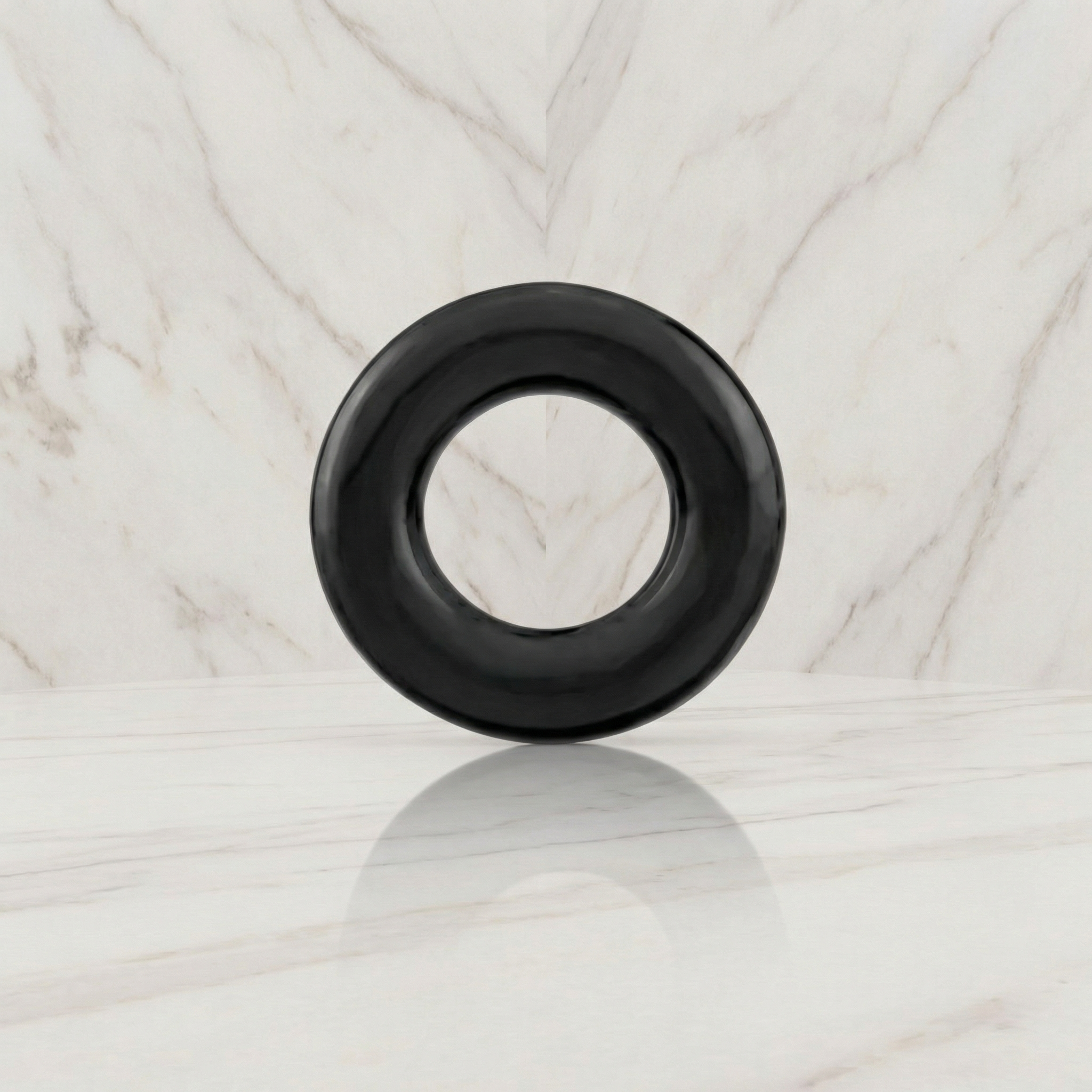 Zwarte cockring rechtop op een marmeren plank tegen een marmeren wand, Kleine cockring
