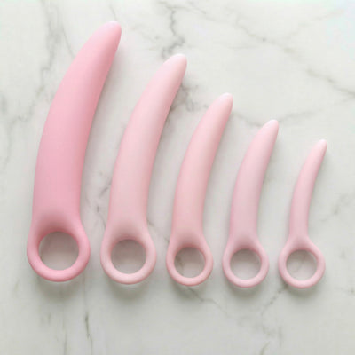 Set van vijf roze siliconen dilators in oplopende maten met vingerring, bovenaanzicht op marmer