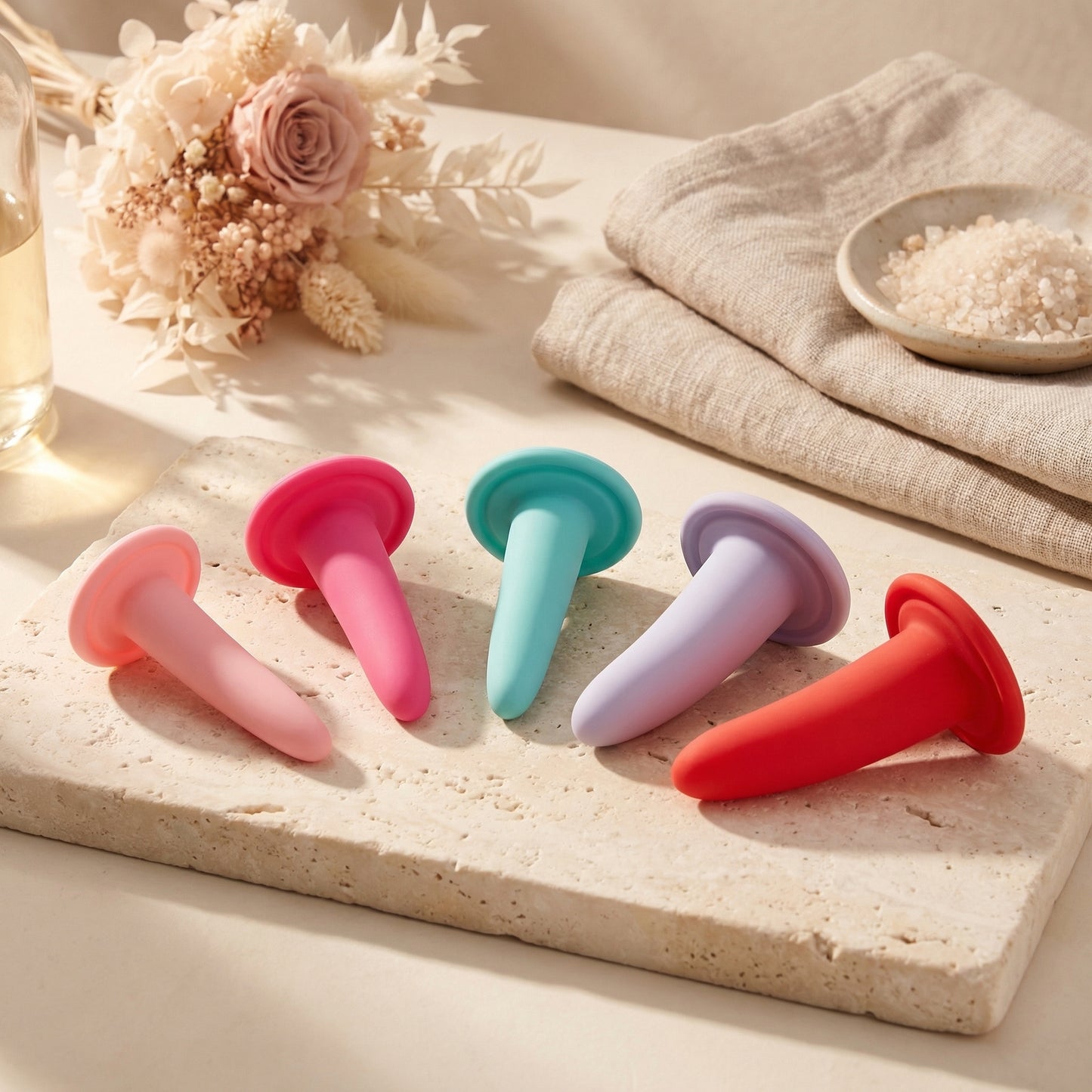 Vijf kleurrijke siliconen vaginale dilatatoren liggend op travertijn, zachte pastelkleuren