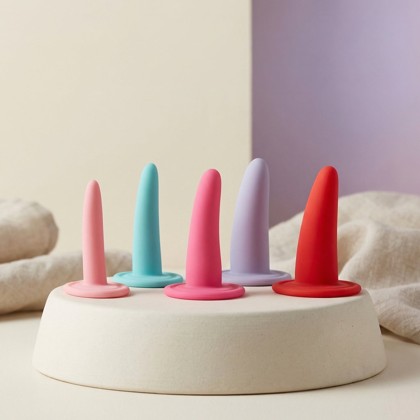 Vijfdelige siliconen dilatorenset in pastelkleuren op podium, oplopende maten voor vaginale training
