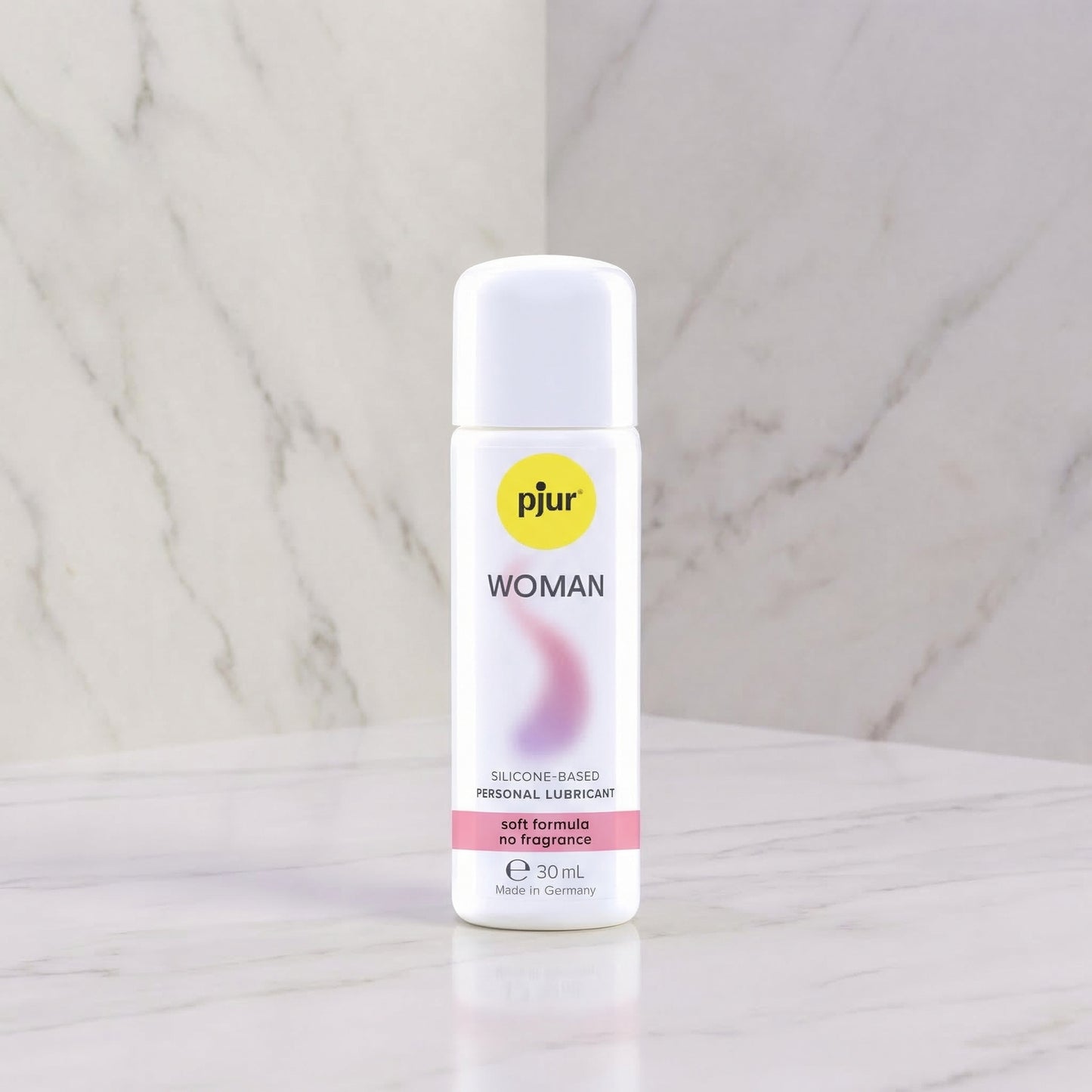 Pjur Woman siliconen glijmiddel 30 ml, witte fles met roze accent, op marmeren achtergrond