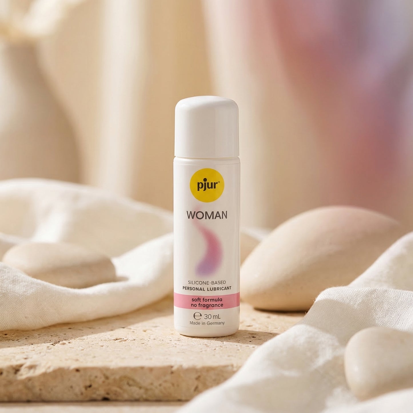 Pjur Woman siliconenbasis glijmiddel 30 ml, witte fles op natuurstenen ondergrond met zachte stoffen