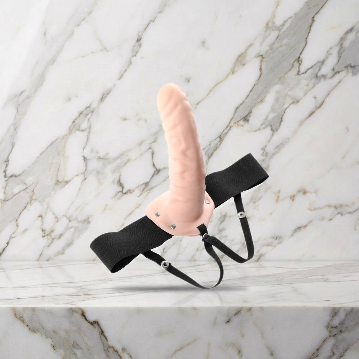 Huidkleurige holle strap-on met zwart harnas op een marmeren plank, maat L-XL