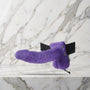 Paarse holle strap-on met balzak en zwarte heupband op een marmeren plank