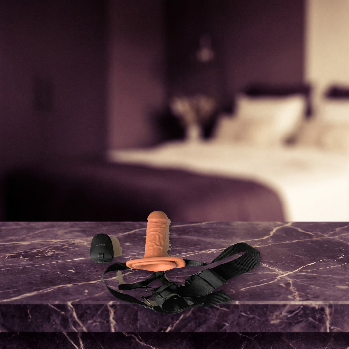 Sfeerbeeld: de holle strap-on met tan dildo, band en afstandsbediening op een donker marmeren nachtkastje