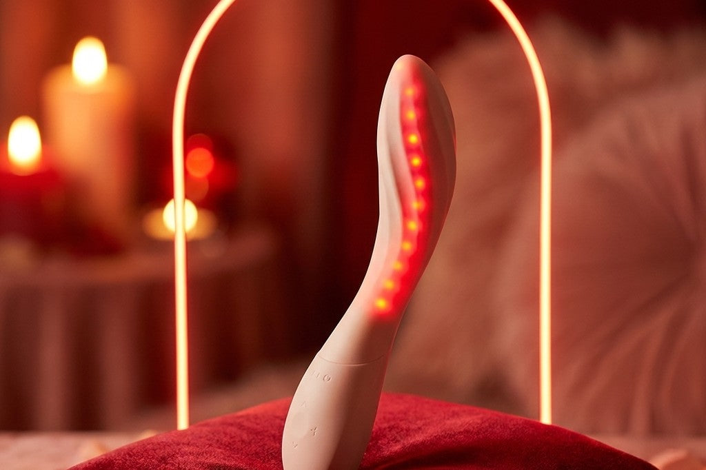LELO Mona Spectra met rood licht op een fluwelen kussen, in een slaapkamer met kaarslicht